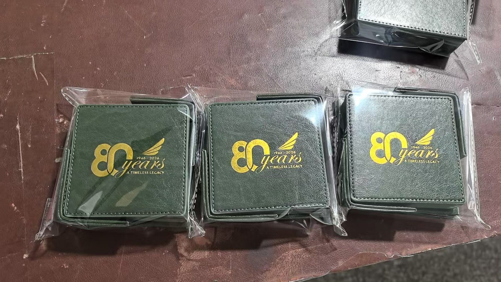 Three green leatherette coasters with gold foil 80th anniversary logo — production photo