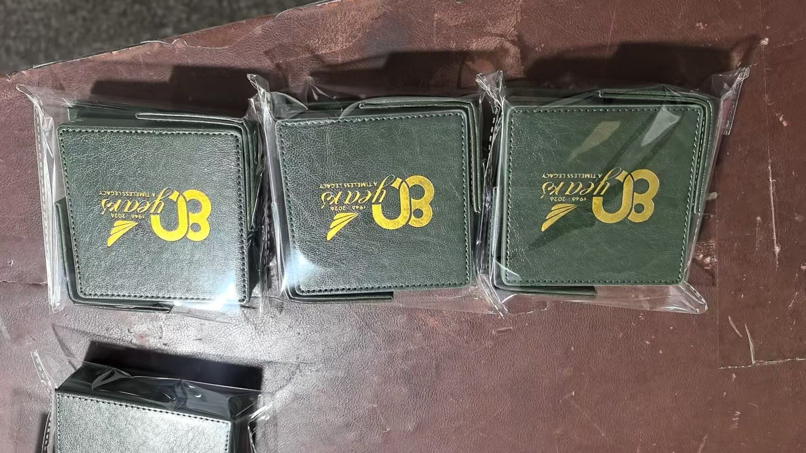 Green leatherette coaster with gold foil 80th anniversary logo — production photo
